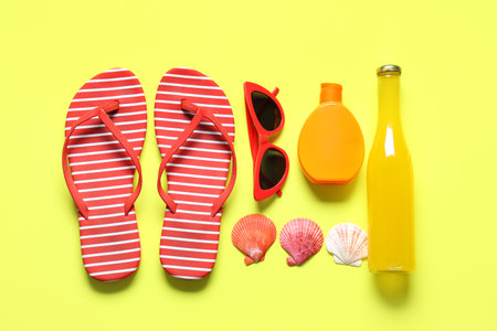 Stylish striped flip-flops with bottle of cocktail, sunglasses, seashells and sunscreen cream on...