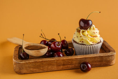 Wooden board with sweet cherry cupcake and spoon of jam on brown backgroundの写真素材