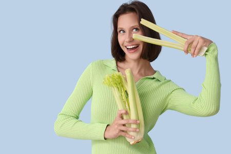 Beautiful young happy woman with fresh celery on blue background. Diet concept