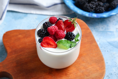 Glass of tasty yogurt with different fresh berries and mint on light blue backgroundの写真素材