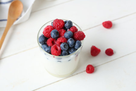 Glass of tasty yogurt with fresh blueberries and raspberries on white wooden backgroundの写真素材