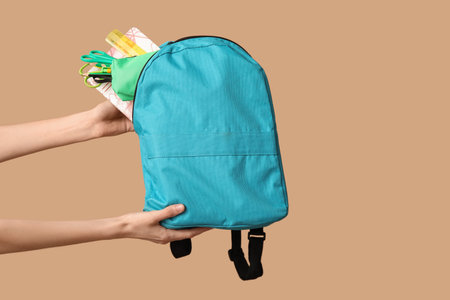 Female hands with backpack and different school supplies on beige background, closeup