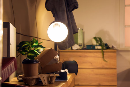 Glowing lamp with garbage on commode in messy office at night, closeup