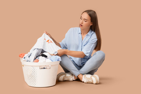 Shocked young woman with stained clothes sitting on beige backgroundの写真素材