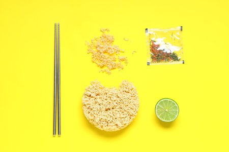 Raw instant noodles with condiment, lime and chopsticks on yellow backgroundの写真素材