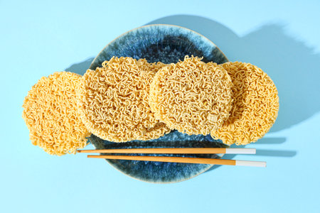 Plate with raw instant noodles and wooden chopsticks on blue backgroundの写真素材