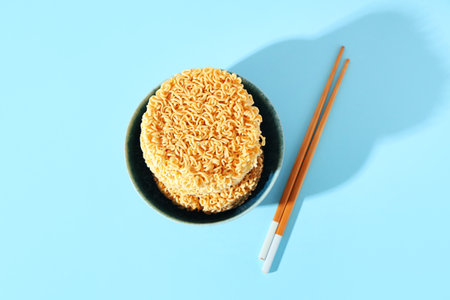 Bowl with raw instant noodles and wooden chopsticks on blue backgroundの写真素材