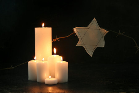 Burning candles with barbed wire and Jewish badge on black background. Day of Remembrance