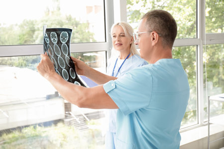 Mature doctors studying MRI scan near window in clinic