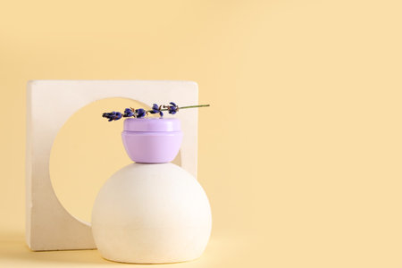 Decorative podiums with jar of cosmetic cream and lavender flowers on yellow backgroundの写真素材