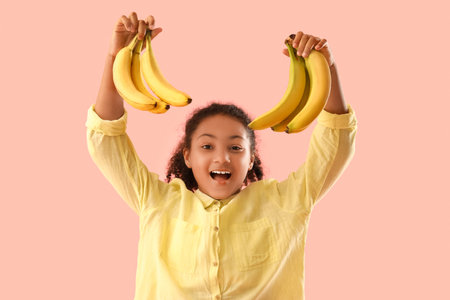 Little African-American girl with bananas on pink backgroundの写真素材