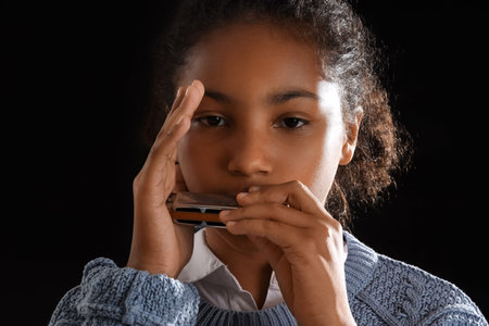 Little African-American girl playing harmonica on dark background, closeup