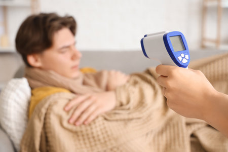 Woman with infrared thermometer and ill man at home, closeup