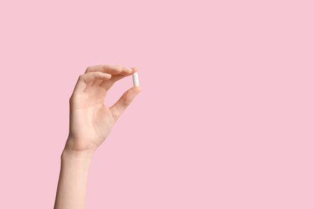 Female hand holding pill on pink backgroundの写真素材