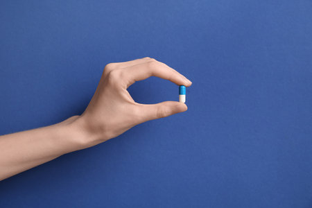 Female hand holding pill on blue backgroundの写真素材