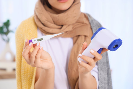 Sick young woman with different thermometers at home