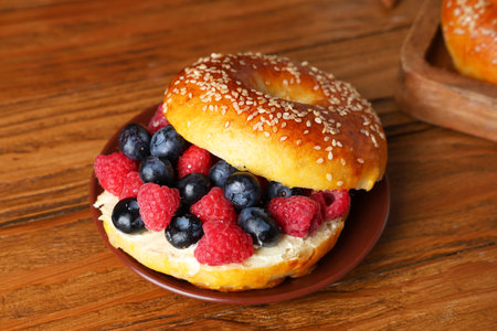 Plate of tasty bagel with butter and berries on wooden backgroundの写真素材