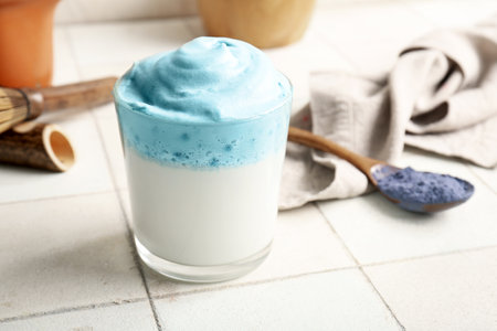 Glass of blue dalgona matcha latte, napkin and spoon on tile table, closeupの写真素材