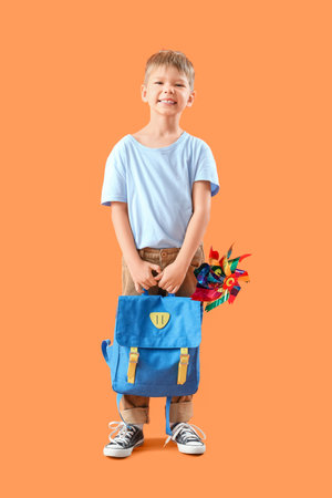 Cute little schoolboy with toy windmill in his backpack on orange backgroundの写真素材