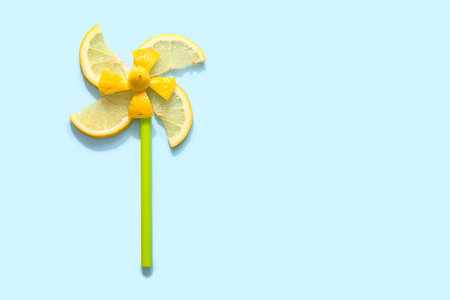 Windmill made of slices of lemon and plastic straw on blue background