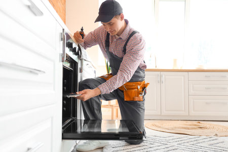 Male technician repairing electric oven in kitchenの写真素材