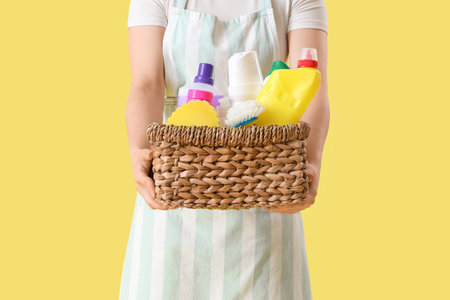 Female janitor with basket of cleaning supplies on yellow background, closeupの写真素材