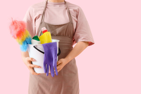 Female janitor with bucket of cleaning supplies on pink background, closeupの写真素材