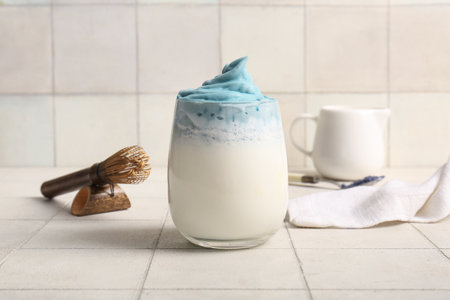 Glass of blue dalgona matcha latte, jug, chasen and napkin on tableの写真素材