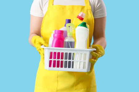 Female janitor with basket of cleaning supplies on blue background, closeupの写真素材