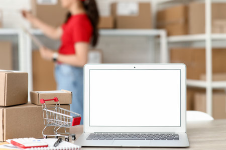 Blank laptop with shopping cart and parcel boxes on table at postal warehouse, closeupの写真素材