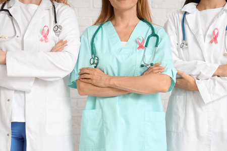 Female doctors with pink ribbons on white brick background, closeup. Breast cancer awareness conceptの写真素材
