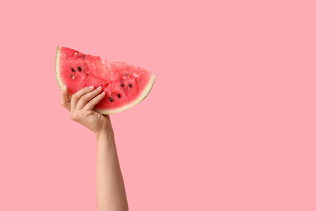 Female hand with slice of sweet watermelon on pink backgroundの写真素材