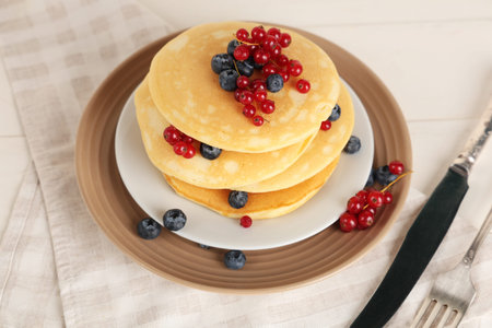 Plate of sweet pancakes with fresh blueberries and red currants on white wooden background