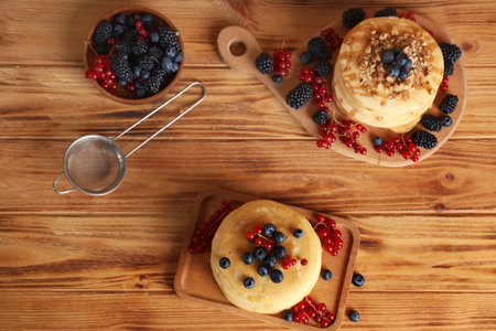 Boards of sweet pancakes with different fresh berries and nuts on wooden backgroundの写真素材