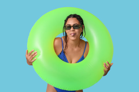 Beautiful young African-American woman in stylish swimsuit with inflatable ring showing tongue on...