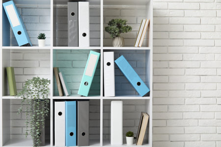 Shelf unit with document folders and plants near white brick wall
