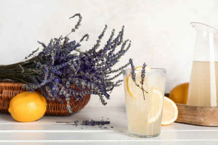 Glass of cold lavender lemonade, pitcher, flowers and lemons on light wooden tableの写真素材