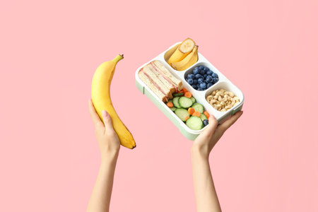 Female hands with school lunch box and banana on pink backgroundの写真素材
