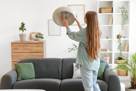 Young woman screwing light bulb into ceiling lamp at home, back viewの写真素材