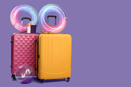 Inflatable rings, suitcases, sunscreen cream and passport with ticket on lilac background. Travel conceptの写真素材