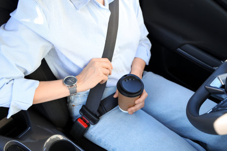 Fastened female driver with coffee cup sitting in car, closeup