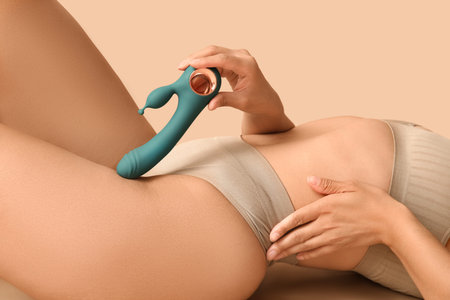 Beautiful young woman in sexy underwear with vibrator lying on beige background, closeup