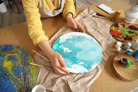 Female artist creating fluid art painting at table in workshopの写真素材