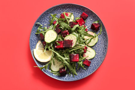 Plate of fresh salad with beet and cucumber on red background