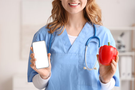 Female nutritionist with bell pepper and mobile phone in office, closeupの写真素材