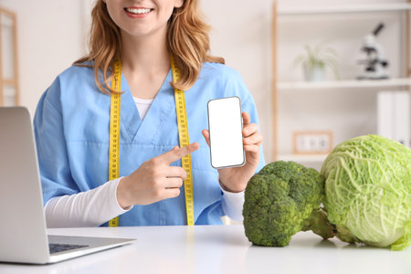 Female nutritionist pointing at blank mobile phone in office, closeupの写真素材
