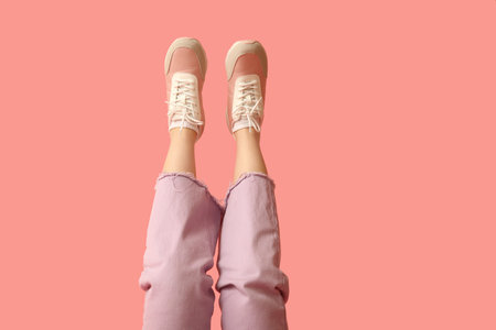 Legs of young woman in stylish sneakers on pink background
