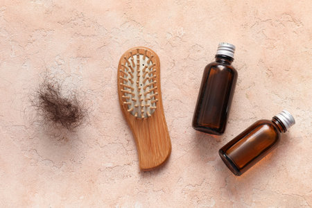 Brush with clump of hair and cosmetic oil on beige background. Hair loss problemの写真素材