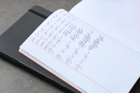 Open copybook with maths formulas and notebook on grunge background, closeup