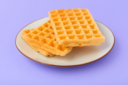 Tasty Belgian waffles in plate on lilac background